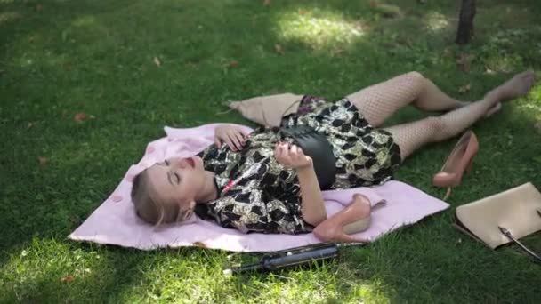 Wide shot careless young woman lying on green lawn in park singing. Sad drunken Caucasian millennial lady with broken heart outdoors on weekend. Problems and procrastination concept. — 图库视频影像