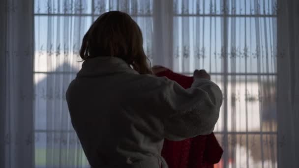 Silhouette of transgender woman in bathrobe choosing dress standing at window indoors. Confident Caucasian LGBTQ person getting dressed in bedroom at home indoors. Individuality and lifestyle. — Video Stock