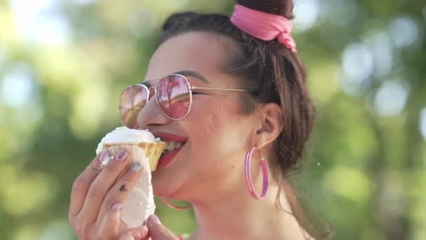 Headshot счастливый радостный Кавказский молодой ретро-женщина с волосами булочки едят вкусные сладкие блины на открытом воздухе улыбаясь. Позитивная красивая брюнетка в солнечных очках наслаждается вкусной едой на открытом воздухе. — стоковое видео
