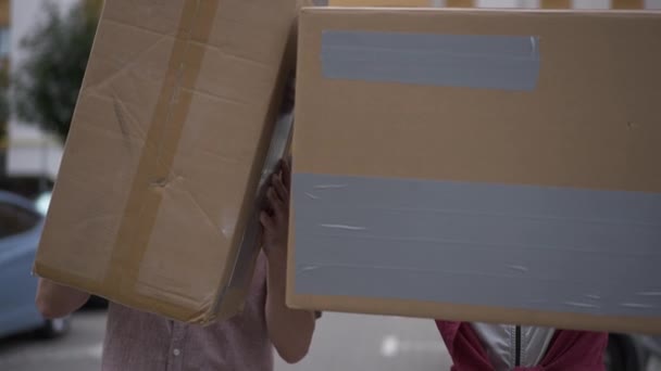 Close-up cardboard boxes with cheerful Caucasian couple appearing emerging in slow motion smiling looking at camera. Positive happy man and woman having fun moving in new apartment. — Stock Video