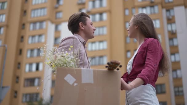 Side view portrait unsatisfied Caucasian couple with cardboard box looking at building turning to each other with dissatisfied facial expression. Unhappy tenants outdoors. Renting and lifestyle. — Vídeo de Stock