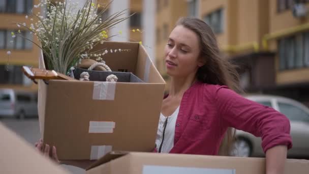 Young slim woman standing on house parking lot as man passing adding heavy cardboard box. Portrait of sad Caucasian tired wife with rude husband moving in new apartment. Slow motion. — Vídeo de Stock