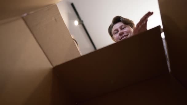 Pohled zevnitř krabice pár otvírá balíček s vzrušeným překvapeným výrazem obličeje. Šťastný kavkazský manžel a manželka obdrží dodávku obdivující online nákup ve zpomaleném filmu. — Stock video