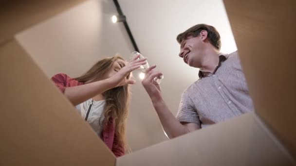 Joyful couple unpacking parcel moving in new apartment gesturing success closing box in slow motion. View from inside cheerful Caucasian man and woman rejoicing relocation. Happiness and joy. — Vídeo de Stock