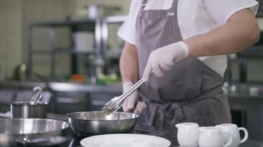 Önlüklü tanınmayan bir aşçı, içerideki ticari mutfakta ananas kızartma tavasında meyve dilimi yapıyor. Profesyonel uzman Kafkas erkek şef restoranda lezzetli bir akşam yemeği hazırlıyor..