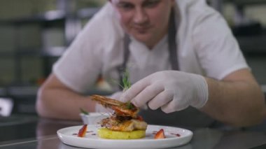 Lezzetli deniz ürünleri tabağı ve bulanık gülümseyen şefin yeşillik süsleme tabağı. Profesyonel Kafkasyalı erkek aşçı restoranın mutfağında yemek hazırlıyor..