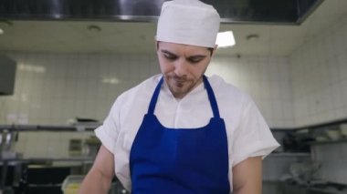 Önden bakan, aşçı üniformalı, alnını ovuşturan, arka plandan ayrılan bir iş arkadaşı gibi düşünen yorgun bir adam. Restoranın mutfağındaki Kafkasyalı aşçının portresi..