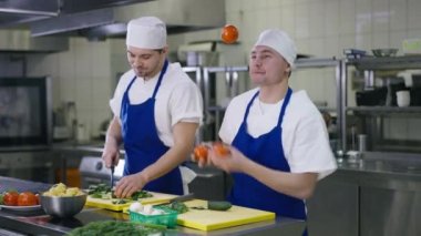 Tasasız neşeli aşçı, domates hokkabazlığı yapıyor, iş arkadaşına salata pişirirken böbürleniyor. Rahatlamış, neşeli beyaz adamın portresi restoranda iş yerinde eğleniyor..