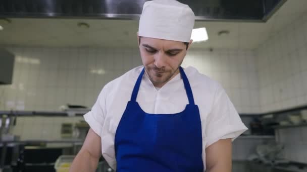 Vista frontale uomo stanco in uniforme cuoco sfregamento fronte pensando come collega di passaggio in partenza sfondo. Ritratto di cuoco caucasico che lavora troppo sul posto di lavoro nella cucina del ristorante. — Video Stock