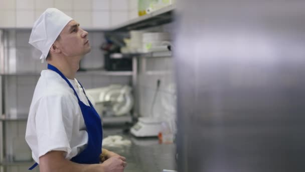 Sidovy porträtt koncentrerad kaukasisk kock välja tillsatser i kommersiellt kök inomhus. Tänksam kock i uniform som står och tänker. Professionalism och service. — Stockvideo