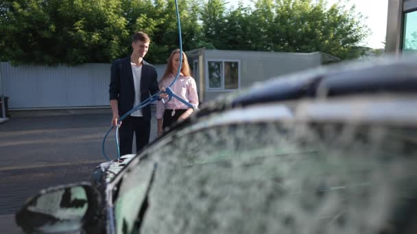 Happy smiling couple standing in sunshine washing car at wash station in slow motion. Positive loving Caucasian boyfriend and girlfriend cleaning vehicle outdoors. Success and lifestyle. — Wideo stockowe