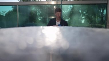 Front view cheerful young man having fun washing car imitating shooting with soap foam in slow motion. Portrait of laughing Caucasian successful guy cleaning automobile shining in sunlight.