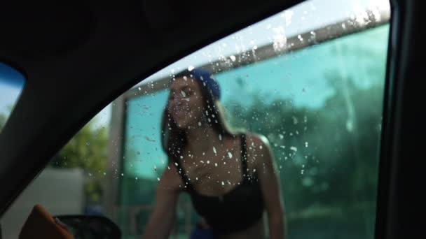 Female hand cleaning car side window with cloth in slow motion. Shooting from inside automobile young slim Caucasian woman washing vehicle at car wash service outdoors. — стокове відео