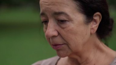 Close-up desperate frustrated senior woman looking away thinking standing outdoors in park. Portrait of sad Caucasian depressed brunette retiree with brown eyes. Sadness and hopelessness concept.