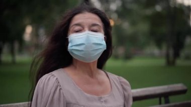 Senior woman taking off coronavirus face mask inhaling fresh air sitting in park outdoors. Portrait of happy relaxed Caucasian retiree looking away smiling enjoying leisure on Covid-19 pandemic.