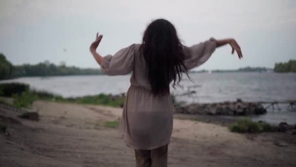 Back view joyful senior Caucasian woman dancing moving hands imitating flying with birds over lake at background. Happy confident lady enjoying leisure outdoors on river bank. — Vídeo de Stock