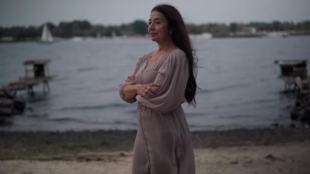 Side view portrait confident senior Caucasian woman standing on windy day at lake shore turning looking at camera smiling. Happy beautiful retiree posing outdoors at river bank. Retirement lifestyle. — Vídeo de Stock