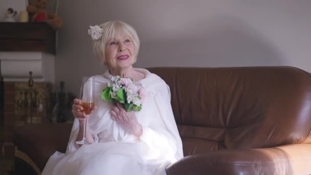Gorgeous elegant senior woman in white wedding dress with bridal bouquet smiling toasting stretching champagne glass at camera. Portrait of happy confident Caucasian bride posing in slow motion. — Video