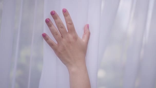 Close-up female Caucasian hand touching white light cloth in slow motion outdoors. Unrecognizable young woman stroking curtain hanging blowing by wind on summer spring day. — 图库视频影像