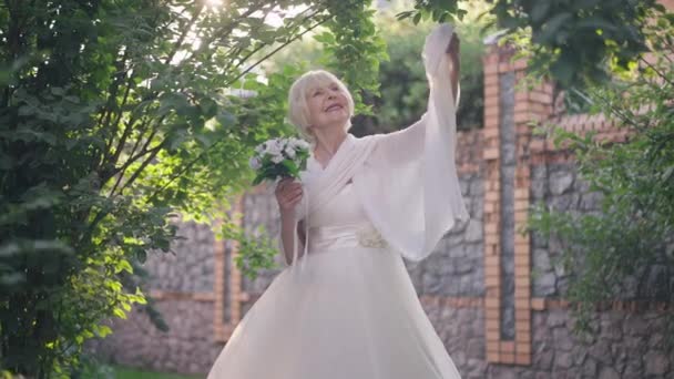 Smiling happy senior bride with grey hair standing in sunshine raising hand with shawl in slow motion. Portrait of confident proud Caucasian woman outdoors in sunlight on wedding day. — Vídeos de Stock