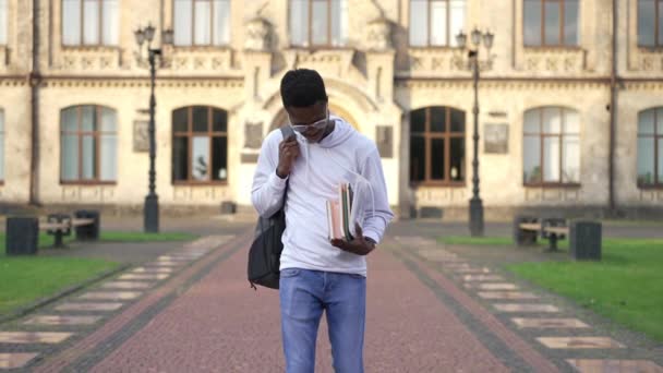 大学キャンパスの屋外フロントビューでスローモーションで歩くインテリジェントアフリカ系アメリカ人学生を確信しています。眼鏡のハンサムな若い男の肖像日当たりの良い朝の書類仕事と散歩. — ストック動画