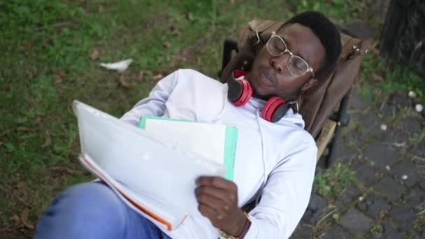 High angle view of concentrated African American genius man lying on bench studying outdoors. Portrait of focused smart intelligent male student learning on college yard. Intelligence and education. — Video