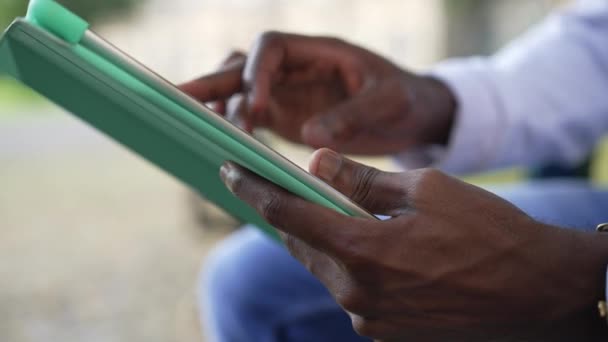 タブレットサーフィンインターネットメッセージをオンラインでアフリカ系アメリカ人男性の手を閉じます。認識できない若い男が屋外でアプリを使って座っている。現代の技術と利便性の概念. — ストック動画