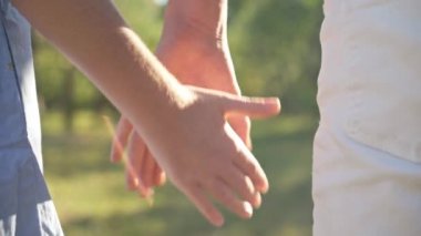 Close-up teenage couple taking hands and walking away in sunshine. Caucasian teen boy and girl holding hands strolling in summer spring park outdoors in sunshine. First love and adolescence concept.