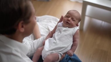 Newborn Caucasian infant shaking in slow motion in hands of happy father indoors at home. Shooting over shoulder of man admiring little cute son. Family and love concept.