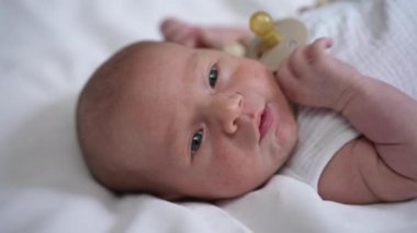 Headshot portrait of cute Caucasian newborn infant with grey eyes lying on bed looking away. Close-up adorable carefree baby kid indoors at home. Tranquility and infancy concept.