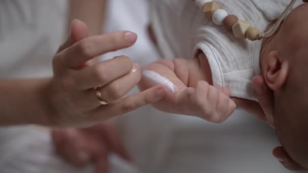 Close-up vrouwelijke vinger wrijven moisturizer in de hand van pasgeboren baby in slow motion. Onherkenbare blanke moeder die thuis voor een zoontje zorgt. Kinderopvang en liefde concept. — Stockvideo