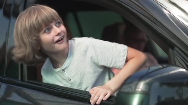 창밖을 내다보고 있는 귀여운 백인 남자 아이의 흥분된 모습 배경에 불분명 한 남자가 차 안에 앉아 있습니다. 화창 한 야외에서 새 차를 타고 있는 아버지와 함께 행복 한 아들. 느린 동작. — 비디오
