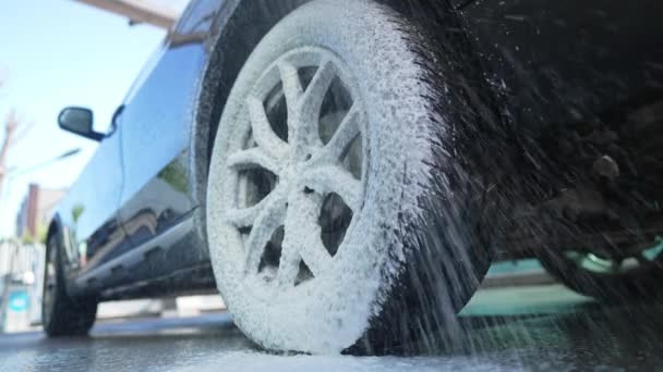 Close-up roda do carro que cobre com espuma branca. Limpeza de pneu de automóvel no serviço de lavagem de carro ao ar livre. Conceito de manutenção e pureza do veículo. — Vídeo de Stock