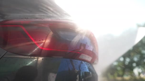 Close-up Auto-Scheinwerfer mit Wasser versprühen in Sonnenstrahlen im Freien. Autowaschen bei Sonnenschein in der Autowäsche. — Stockvideo