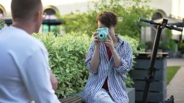 Şehir caddesinde oturan yetenekli genç kadın fotoğrafçı. Güzel gülümseyen beyaz fotoğrafçının portresi ağır çekimde fotoğraf çekiyor. Yaşam tarzı ve eğlence konsepti.