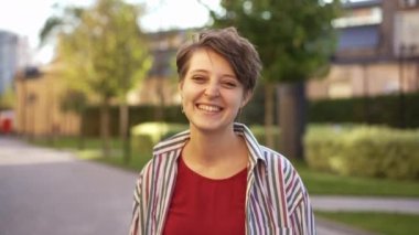 Muhteşem beyaz kadın kameraya bakıp gülümsüyor. Şehir caddesinde güneşin altında dikiliyor. Yavaş çekimde poz veren mutlu, kendine güvenen, ince bir kadının portresi. Kamera hareket ediyor.