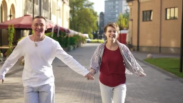 Spännande bekymmerslösa unga par som håller händerna i slow motion i solsken på stadens gata. Front view dolly skott av avslappnad kärleksfull vit man och kvinna har kul dejta utomhus vid solnedgången. — Stockvideo