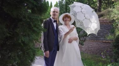 Gelinlik ve takım elbiseli, açık havada güneş şemsiyesiyle poz veren romantik, son sınıf aşığı çift. Mutlu beyaz erkek ve kadının portresi. Yaz günü evleniyorlar. Gülümsüyorlar..