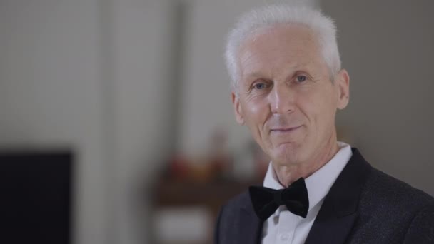 Retrato do noivo sênior feliz girando olhando para a câmera sorrindo em câmera lenta em pé à direita. Homem caucasiano bonito confiante com cabelos grisalhos em blazer elegante e gravata borboleta posando no casamento. — Vídeo de Stock