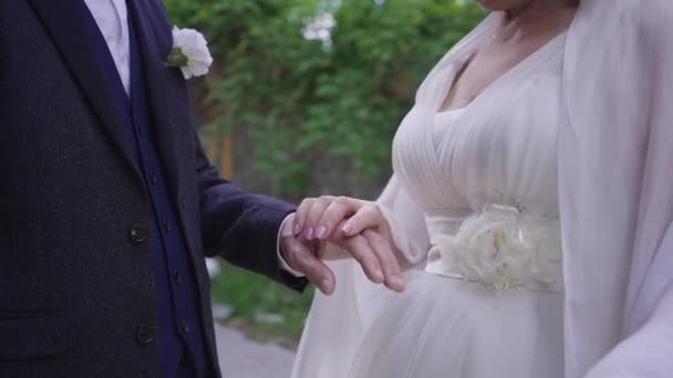 难以辨认的高级新娘和新郎手握着手，慢吞吞地站在室外。喜庆的白种人夫妻在结婚当天牵着手。浪漫与享受. — 图库视频影像