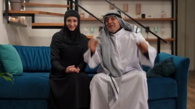 Geniş açılı Orta Doğulu kadın ve erkek, evlerinde futbol maçı izlerken tezahürat yapıyorlar. Gülümseyen heyecanlı karı koca spor hayranları hafta sonunun keyfini çıkarıyorlar. Canlı kamera yakınlaştır.