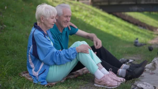 Iubind fericita soție senior îmbrățișând soțul stând pe pajiște verde de vară hrănind păsările în mișcare lentă. Frumos caucazian femeie cu frumos om în aer liber se bucură de petrecere a timpului liber. — Videoclip de stoc