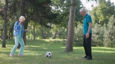 Açık havada güneşli yaz çimlerinde ağır çekimde futbol oynayan heyecanlı yaşlı adam ve kadın. Mutlu Kafkasyalı emekliler bahar parkında spor ve eğlencenin tadını çıkarıyorlar. Yaşam tarzı ve mutluluk.