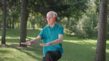 Kendine güvenen kıdemli sporcu dizlerini yavaşça kaldırarak gülümsüyor. Kafkas formundaki, kulaklıklı bir adamın portresi güneşli bir bahar günü açık havada antrenman yapıyor..