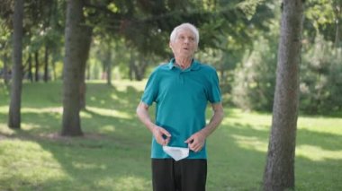 Kafkasyalı üst düzey bir adamın koronavirüs maskesini çıkarırken, parkta havayı süzerken, ağır çekimde sırıtırken orta boy bir fotoğrafı. Mutlu emekliler. Yaz tatilinin tadını çıkarın. Dışarıda salgın var..