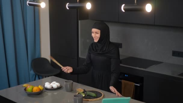Radostná krásná žena ze Středního východu se baví vařením zdravého salátu v kuchyni doma. Portrét veselé štíhlé půvabné dámy zpívající v dřevěné lžíci tanec uvnitř těší víkend volný čas. — Stock video
