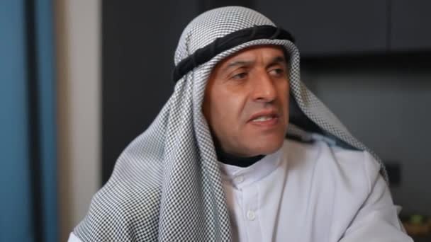 Close-up portrait of angry Middle Eastern man looking at camera with dissatisfied facial expression. Troubled irritated annoyed guy in traditional clothing posing indoors in kitchen at home. — Stock Video