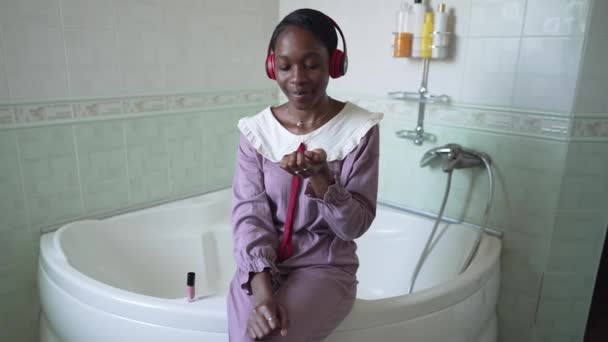 Vue de face portrait de la jeune femme afro-américaine confiante vantant vernis à ongles au ralenti souriant en regardant la caméra. Belle dame mince en pyjama posant au ralenti dans la salle de bain vantant. — Video