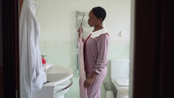 Sisi melihat wanita muda mencoba gaun di kamar mandi berpikir di pagi hari bersiap-siap. Potret wanita Afrika-Amerika langsing memilih pakaian di dalam rumah. Konsep kecantikan dan mode. — Stok Video