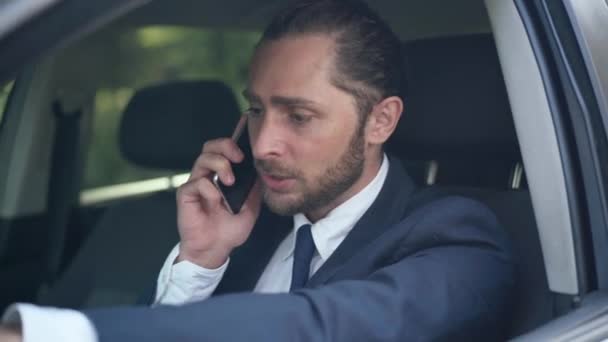Kızgın genç sakallı adam telefonda bağırarak konuşuyor ve arabada tartışıyor. Şoför koltuğunda oturan, akıllı telefonda tartışan kızgın, beyaz, sorunlu işadamının portresi. Öfke ve sorunlar. — Stok video